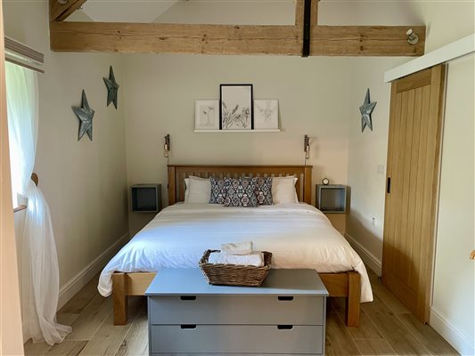 Super king bed with white bed linen and a grey chest of drawers at the foot.